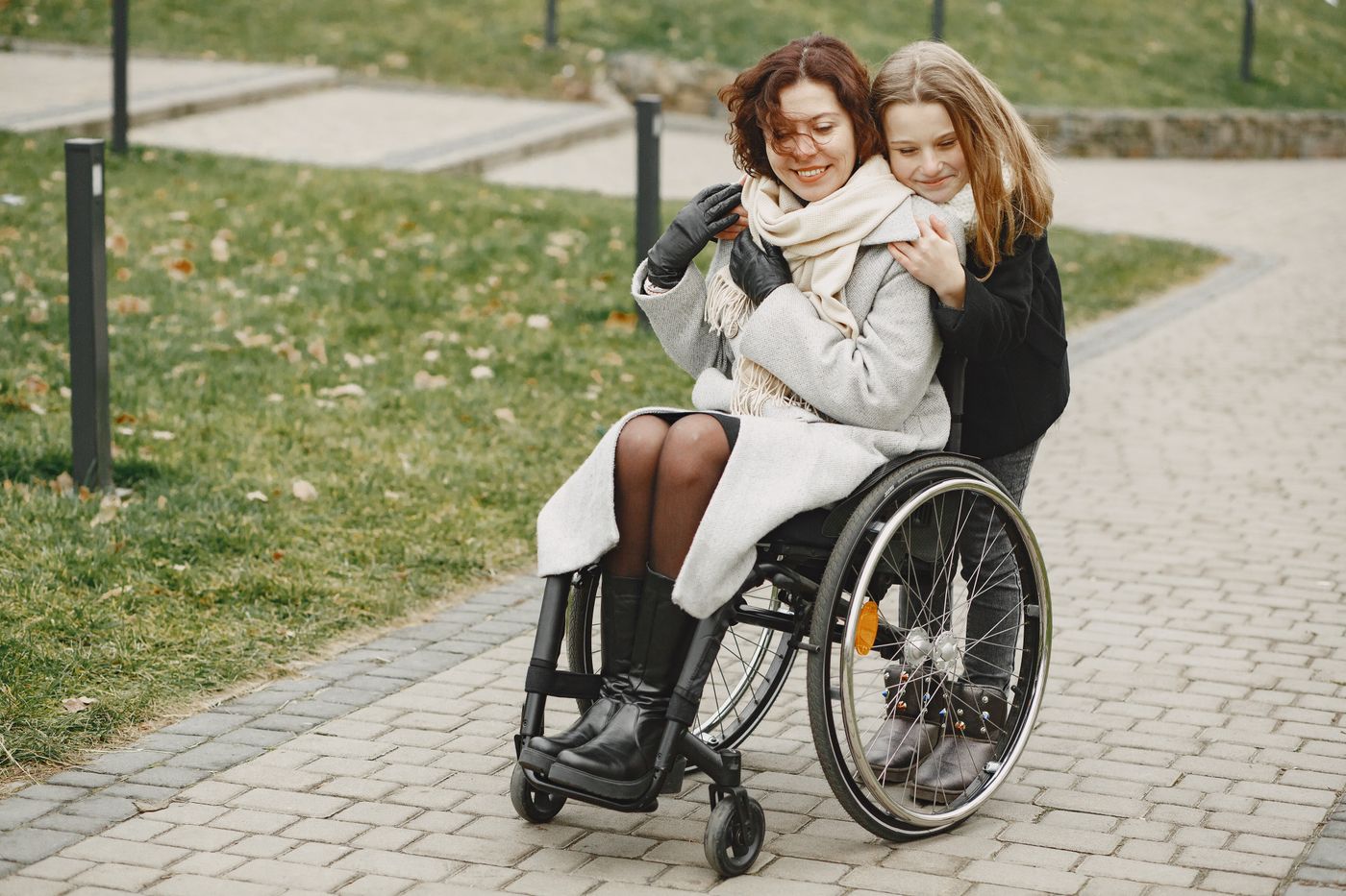A young person embracing their parent, who uses a wheelchair, in a park
